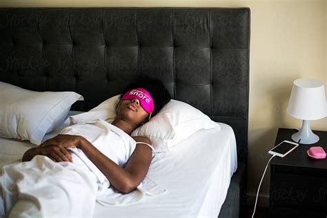 Young Ethnic Lady In Bright Pink Sleeping Mask On Comfortable Bed In Hotel Room By Stocksy