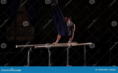 Male Gymnast Acrobat Performs Handstand On Parallel Bars In A Dark Room