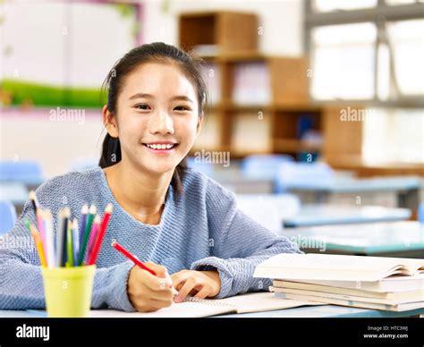Happy Asian Elementary School Student Studying In Classroom Looking At