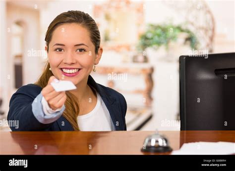 Young brunette hotel receptionist with friendly smile handing over key