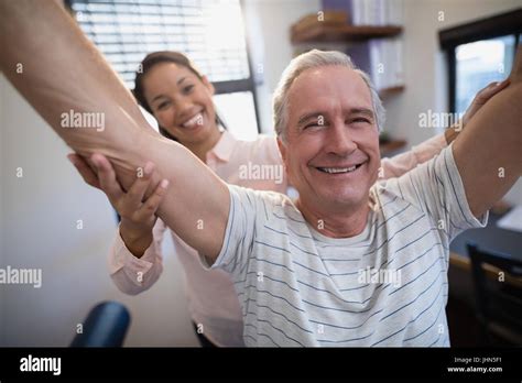 Portrait Of Smiling Senior Male Patient And Female Doctor With Arms Raised At Hospital Ward