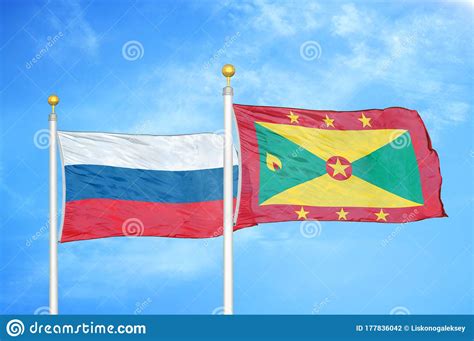 Russia And Grenada Two Flags On Flagpoles And Blue Cloudy Sky Stock