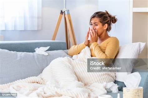 아픈 여자독감여자는 감기에 걸렸습니다 조직으로 재채기 두통 바이러스 의약품 젊은 여자 감염 에 감기 불고 그녀의 코 에 손수건 소파에 앉아 두통을 가진 아픈 여자 가정