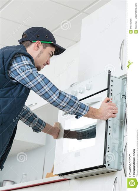 Young Repairman In Overall Installing Brand New Oven In Kitchen Stock