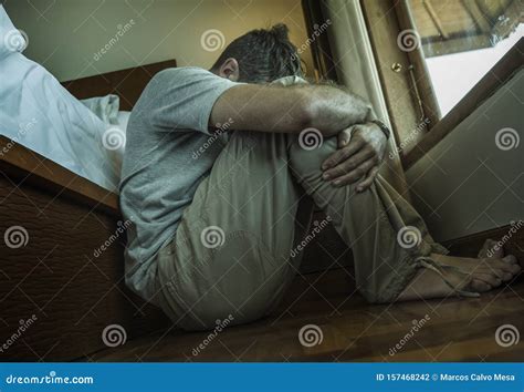 Young Depressed And Desperate Man Sitting On Bedroom Floor Next To Bed