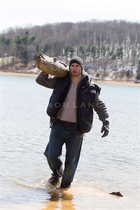 Rugged Man Carrying A Large Log Out Of The Water During The Winter