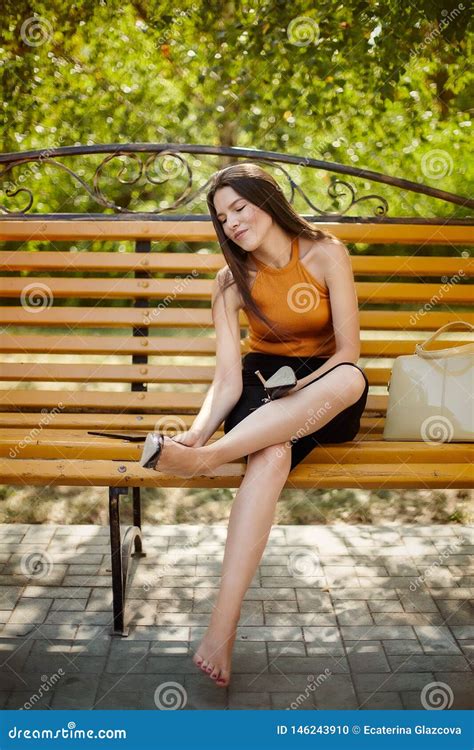 the girl tired of heels takes off her shoes from her feet and sits barefoot on a park bench
