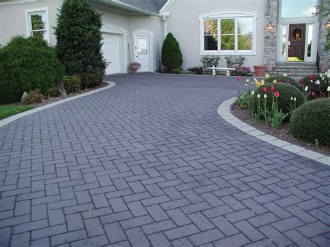 A Driveway With Brick Pavers And Flowers In The Front Yard Leading To