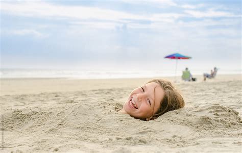 Laughing Girl Buried In Sand At Beach By Stocksy Contributor Brian