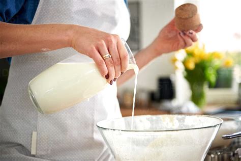 Woman Pouring Milk Into Mixing Bowl In Kitchen Stock Photo