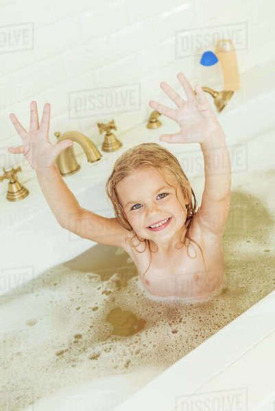 Adorable Babe Girl Raising Hands And Smiling At Camera While Sitting In Bathtub Stock Photo