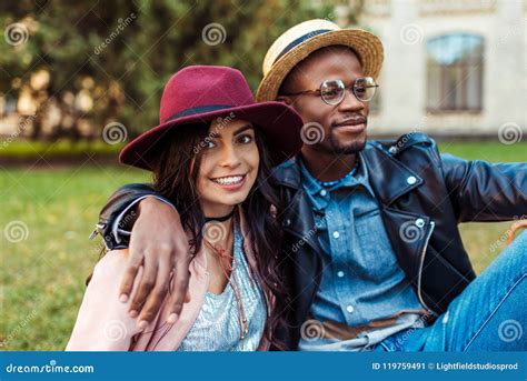 Retrato De Pares Interraciales Preciosos En Los Sombreros Que Se Sientan En Una Hierba En Imagen
