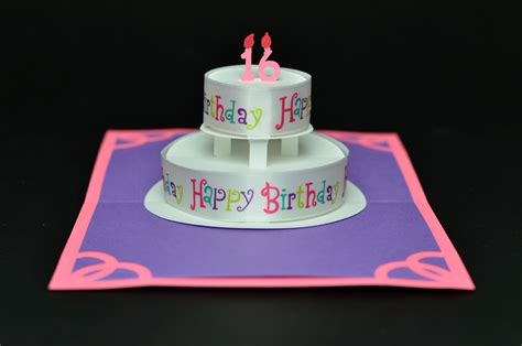 Two Tiered Birthday Cake Sitting On Top Of A Purple And Pink Card