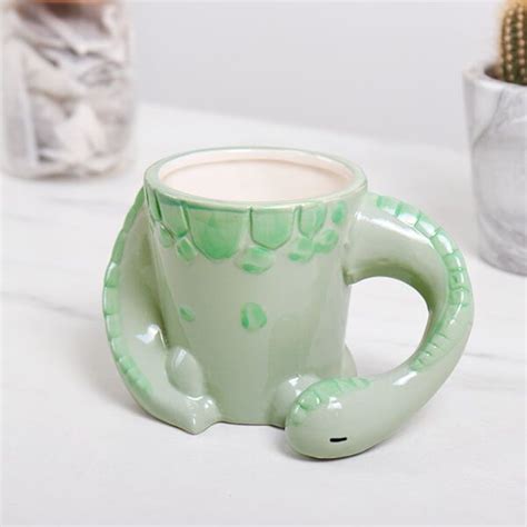 A Green Ceramic Mug With A Lizard Design On It And A Cactus In The