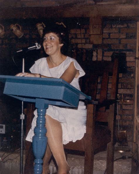 A Woman Sitting At A Blue Table With A Microphone In Her Hand And Wearing Red Shoes