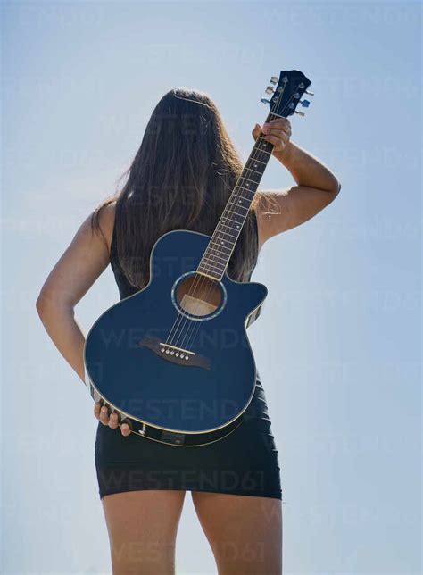 A Teenage Female Guitarist Holds An Acoustic Guitar To Her Back Against