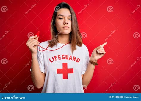 Young Beautiful Brunette Lifeguard Girl Wearing T Shirt With Red Cross Using Whistle Pointing