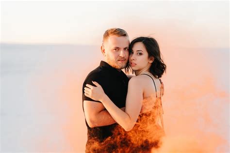 Premium Photo Guy And A Girl In Black Clothes Hug And Run On The White Sand With Orange Smoke