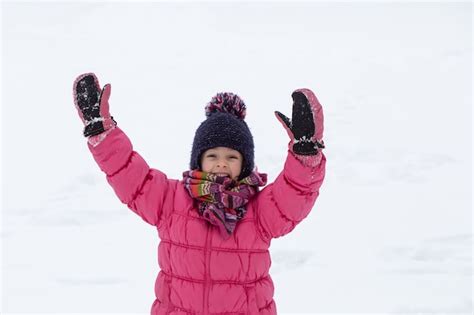 Милая маленькая девочка в розовой куртке и шляпе играет в снегу