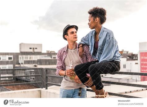 Young Couple Clinking Beer Bottles On Rooftop A Royalty Free Stock