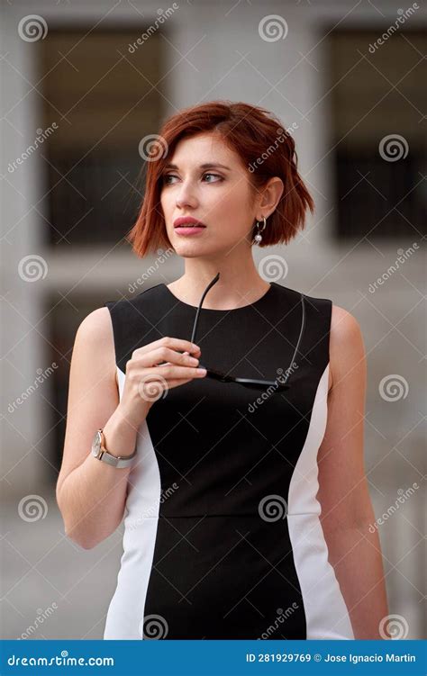 portrait of businesswoman with red hair taking off her sunglasses in the street stock image