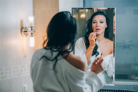 Young Beautiful Woman Brunette In The Bathroom And White Bathrobe Making Make Up Near Mirror