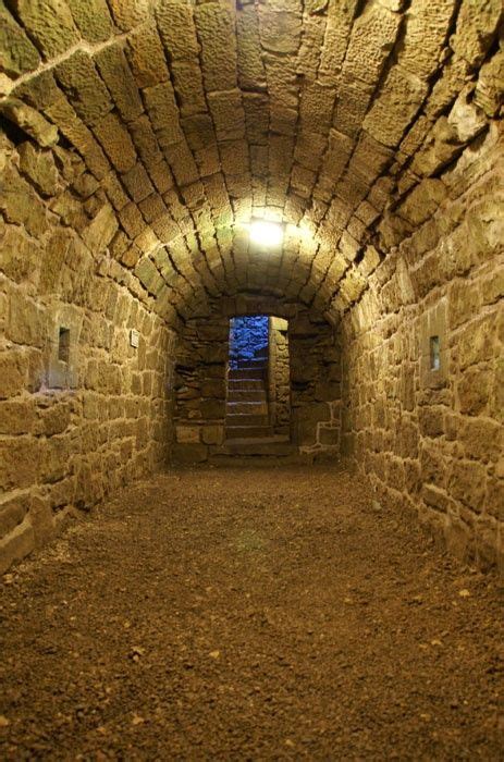 A Tunnel With Stone Walls And Steps Leading Up To The Light At The End