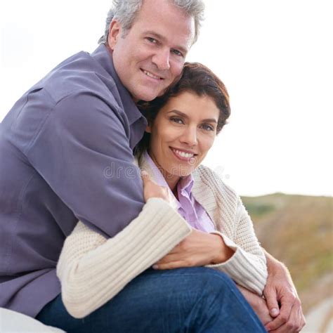 Appreciating One Another A Mature Couple Hugging One Another While Sitting On A Sand Dune