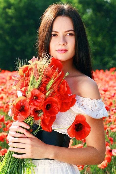 a beautiful woman holding a bunch of red flowers in her hand and looking at the camera