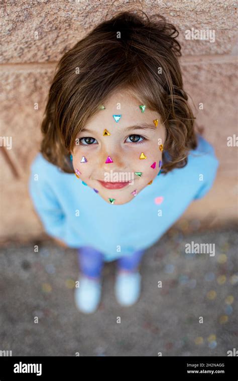 Adorable Girl With Confetti Sticking On Face Standing In Front Of Wall