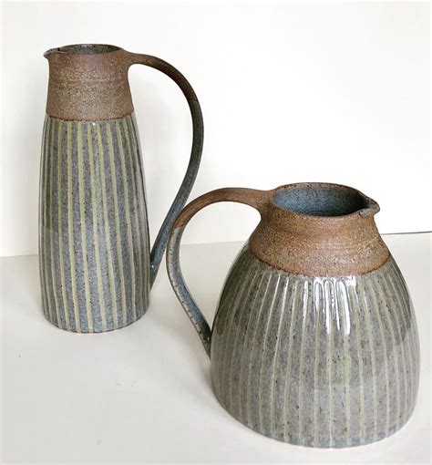 Two Gray And White Striped Pitchers Sitting Next To Each Other On Top Of A Table