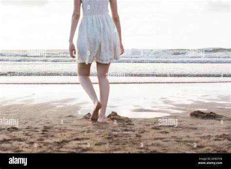Young Woman Wearing White Dress Walking Barefoot On Sand At Beach