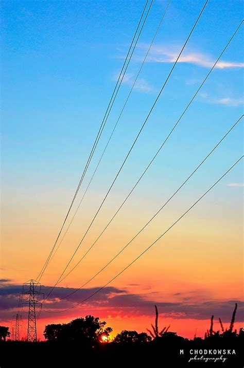 The Sun Is Setting Behind Power Lines And Telephone Poles In The