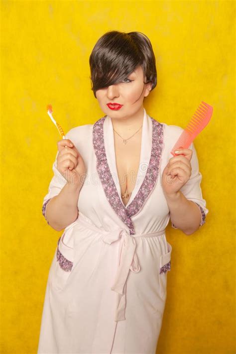 cute chubby girl in a pink robe stands with a comb and toothbrush on a yellow background in the