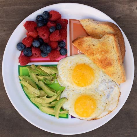 A White Plate Topped With Eggs Toast And Fruit On Top Of A Wooden Table