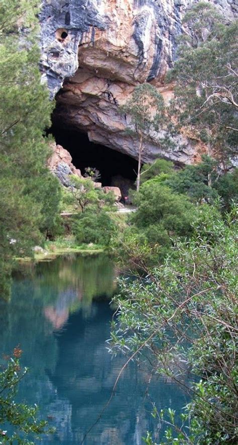 The Water Is Blue And There Are Trees In Front Of It With An Open Cave