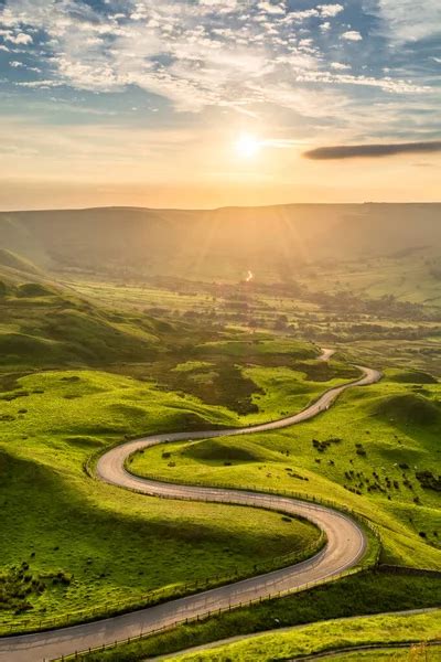 A Long And Winding Road Passing Through Green Hills At Sunset Stock