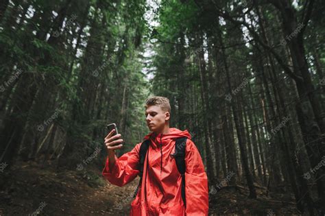Premium Photo Serious Handsome Young Man In A Red Raincoat Uses A Smartphone On A Hike