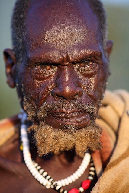 An Old Man With A Beard And Beads On His Neck Is Looking At The Camera