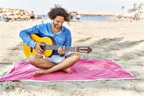 Young Hispanic Man Playing Classical Guitar Sitting On Sand At The