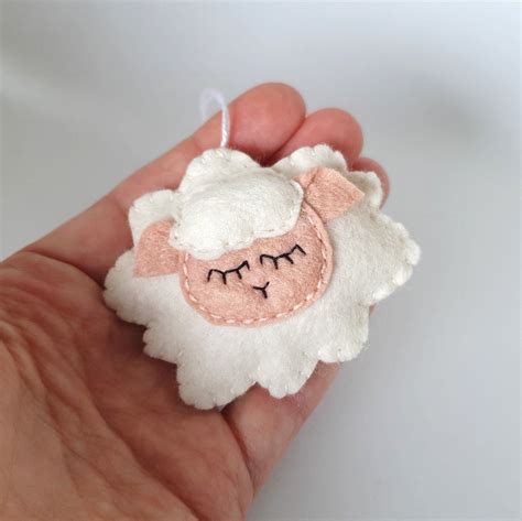 A Hand Holding A White Sheep Ornament With Black Eyes And Pink Wool On It
