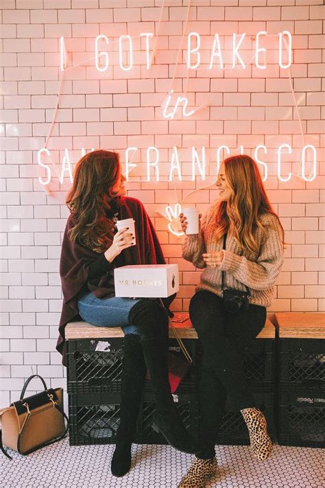 Two Women Sitting On A Bench In Front Of A Brick Wall With Neon Lights