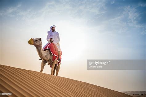 Man Wearing Traditional Middle Eastern Clothes Riding Camel In Desert
