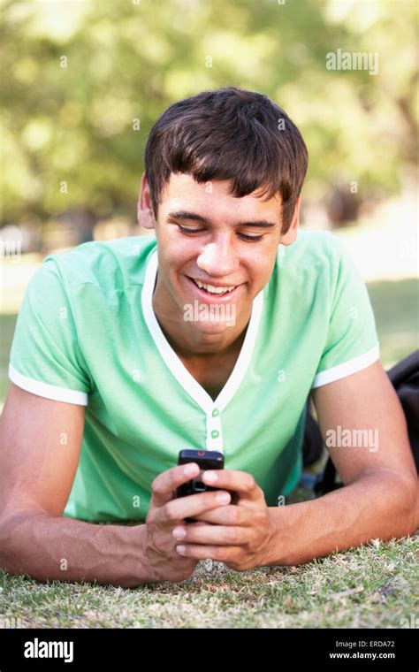 Teenage Boy Laying In Park Reading Text Message On Mobile Phone Stock