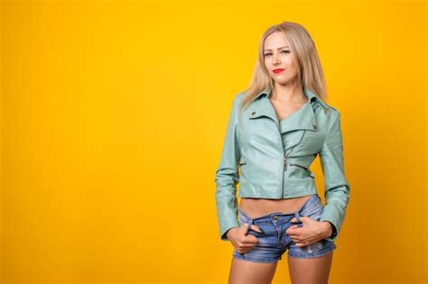 Сексуальная молодая девушка в кожаной куртке и коротких джинсовых шортах на желтом Премиум Фото