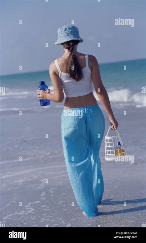 Back View Of Female Long Brunette Hair Wearing Blue Sunhat Cropped White Vest Top And Blue