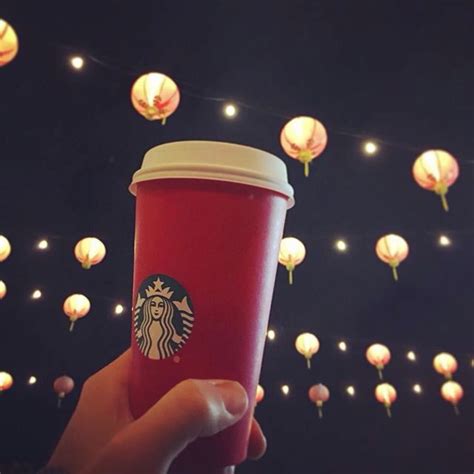 Someone Holding Up A Starbucks Cup With Lanterns In The Sky Behind It
