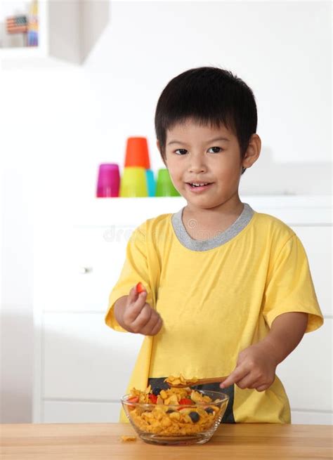 Little Asian Boy Eating Breakfast On Wooden Table In Home Stock Photo