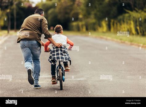 Vista Trasera De Un Niño En Bicicleta Mientras Su Padre Recorre