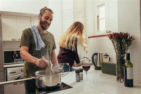 Happy Man Cooking Food While Woman Washing Dishes In Kitchen Couple